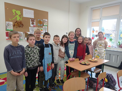Zdjęcie dzieci stojących za stołem na którym stoją 2 talerze z kanapkami.
