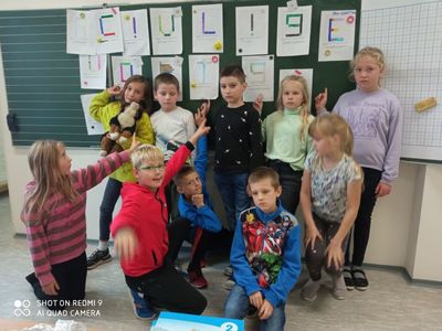 Uczniowie klasy drugiej stojący przy tablicy i wskazujący kartki z rozszyfrowanymi literami.