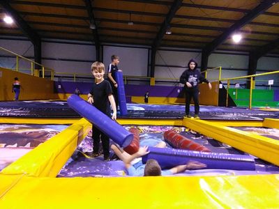 Zdjęcie przedstawiające cztery młode osoby bawiące się na hali z trampolinami.