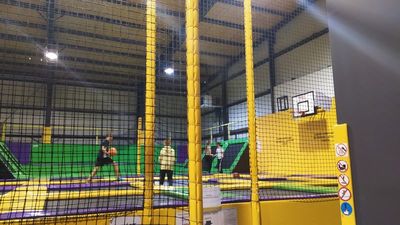 Zdjęcie hali sportowej, parku trampolin. W tle uczniowie skaczący na trampolinach.