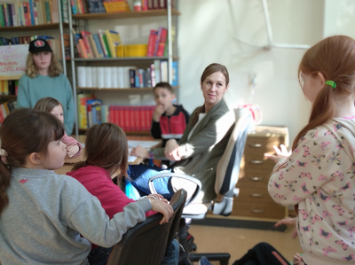 Dziewczynka pokazuje kolegom  za pomocą gestów i mimiki  tytuł książki.
