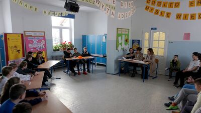 Zdjęcie zawodników i jury turnieju siedzących przy stolikach szkolnych.