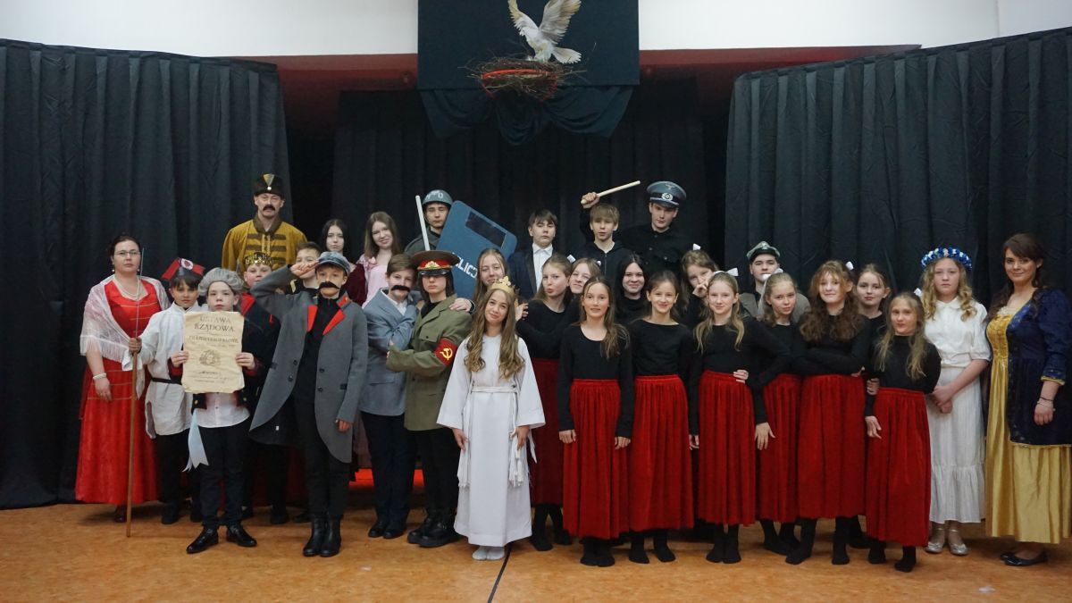 Grupa uczniów wraz z nauczycielami w strojach historycznych na scenie.