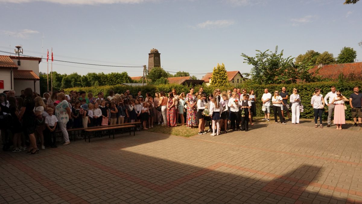 Grupa uczniów i rodziców na placu przed budynkiem szkoły.