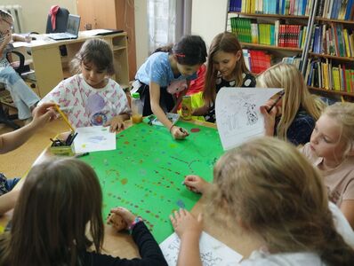 Grupa uczniów w bibliotece tworzy plakat składający się z kropek.