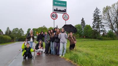 Grupa uczniów wraz z nauczycielką stoi przy tablicy na wjeździe do miejscowości Wrzesina.