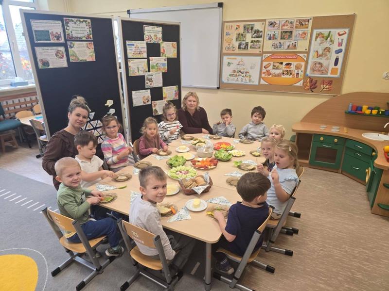 Uczniowie siedzą za stołem, na którym ustawione są talerze ze zdrowym jedzeniem.