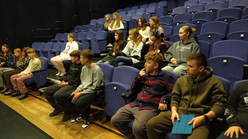 Grupa uczniów siedzący na widowni w sali teatralnej.