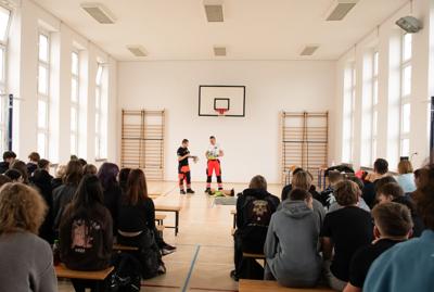  Ratownicy medyczni demonstrują młodzieży na fantomie zasady udzielania pierwszej pomocy przedmedycznej na sali gimnastycznej.