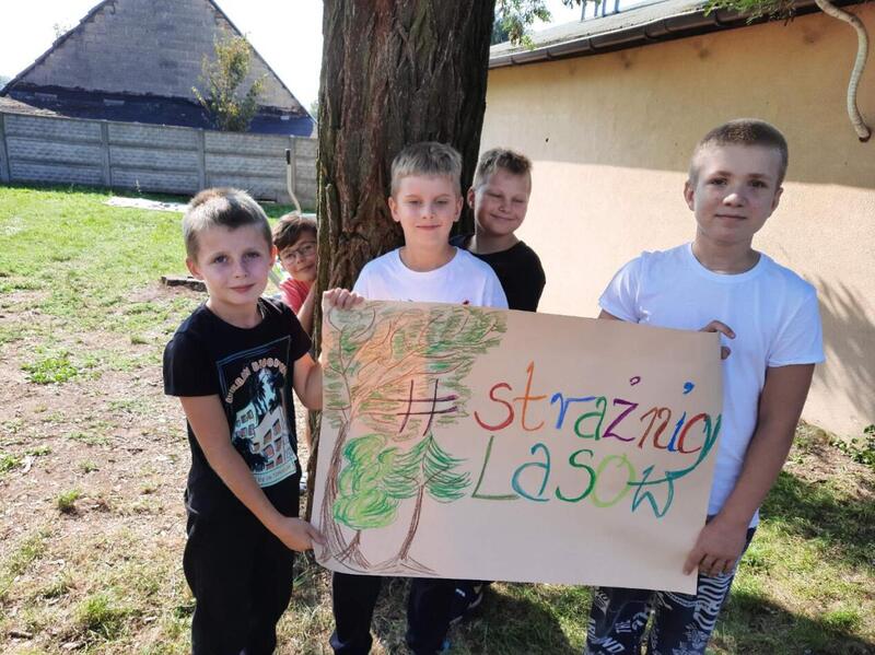 Czterech uczniów na tle drzewa z banerem "Strażnicy lasu"