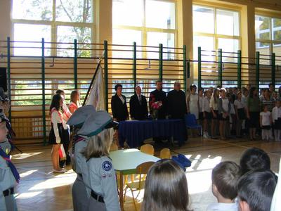 Uroczystość na sali gimnastycznej szkoły. Poczet sztandarowy, dyrekcja szkoły oraz zaproszeni goście