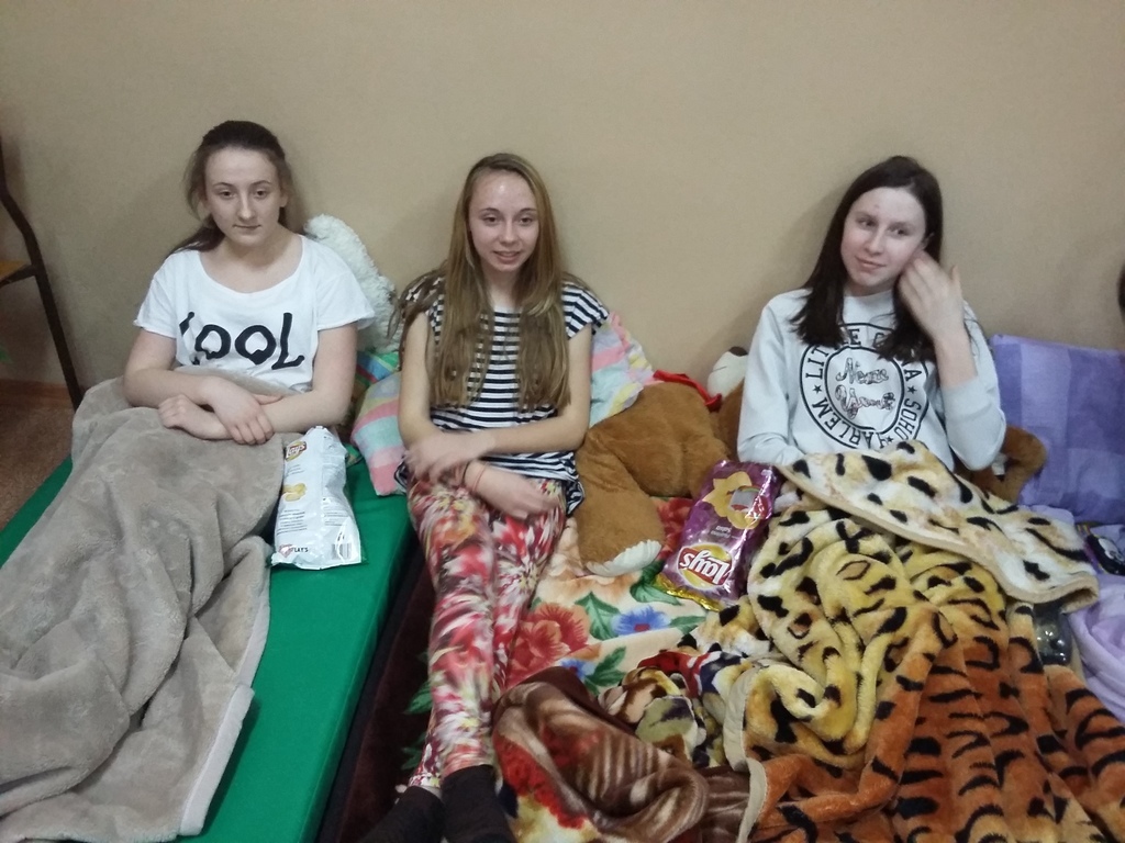 Uczniowie nocujący w szkole owinięci w koce oczekują na seans filmowy.