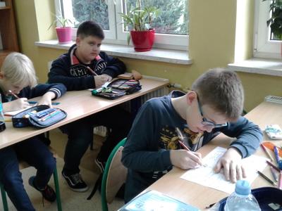 Trzech uczniów rysujących na białych kartkach.