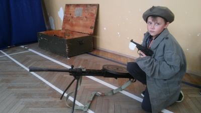 Dziecko ubrane w beret i zieloną kurtkę prezentuje eksponaty militarne.