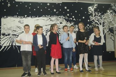 Grupa uczniów na scenie, jeden z chłopców trzyma mikrofon