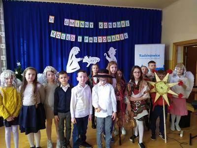 Grupa uczestników konkursu pastorałek na tle sceny