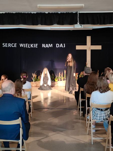 Scena z krzyżem, na scenie dwie osoby w czarnych strojach. Przedstawienie Wielkanocne.