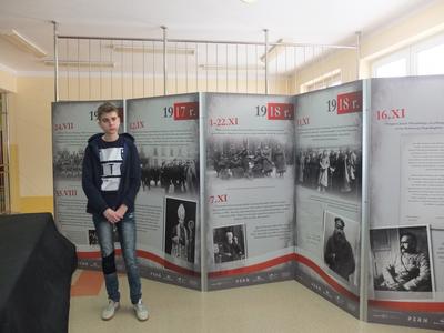 Chłopiec stojący na tle parawanu z informacjami o niepodległości.