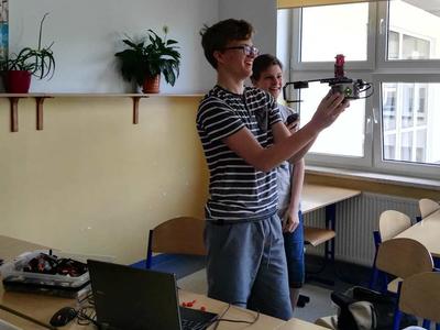 Dwóch chłopców w sali lekcyjnej. Jedn trzyma robota