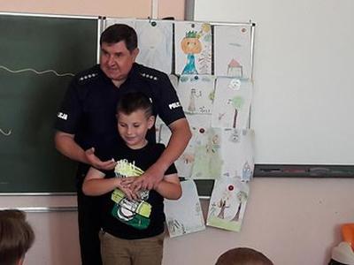 Policjant stojący za chłopcem trzyma go za rękę.