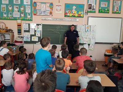 Dzieci słuchają policjanta stojącego przy tablicy 
