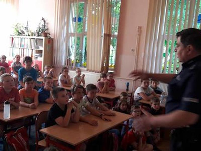 Spotkanie z policjantem. Policjant i dzieci siedzące w ławkach.
