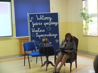 Urszula Ciężka siedzi na krześle i czyta książkę do mikrofonu