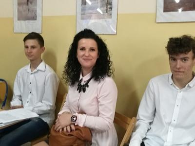 Nauczycielka wraz z dwoma uczniami siedząca przy ścianie.