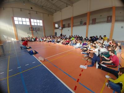 Dzieci w hali sportowej. Ratownik prezentuje udzielanie pierwszej pomocy.