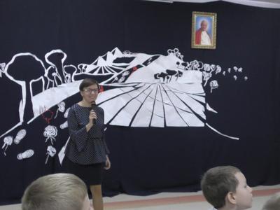 Dyrektor szkoły na tle sceny. Na ścianie wisi obraz Jana Pawła II.