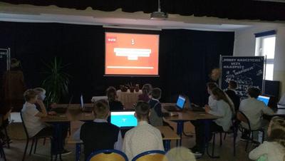Dzieci siedzą. Przed nimi ekran z wyświetloną prezentacją