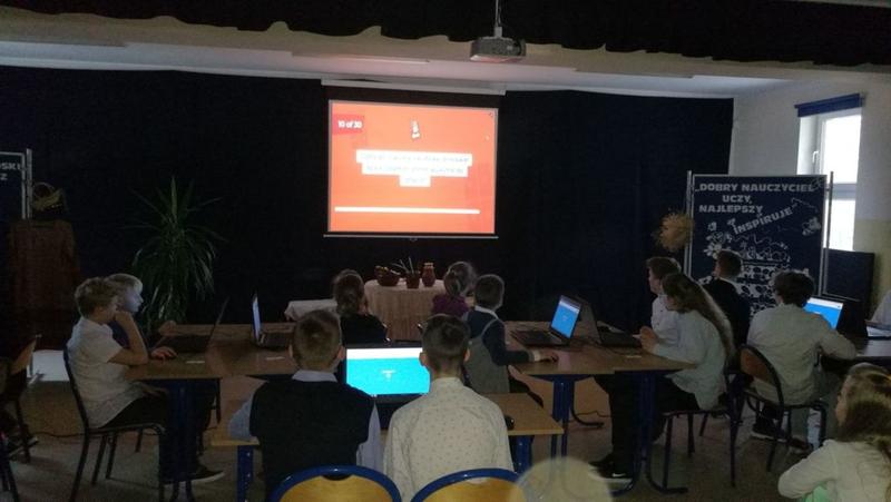 Dzieci siedzą. Przed nimi ekran z wyświetloną prezentacją