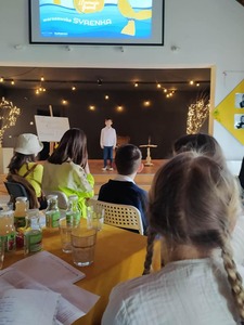 Zdjęcie. Widok ogólny sali. Widzowie słuchają występu. Na scenie jeden z uczestników.