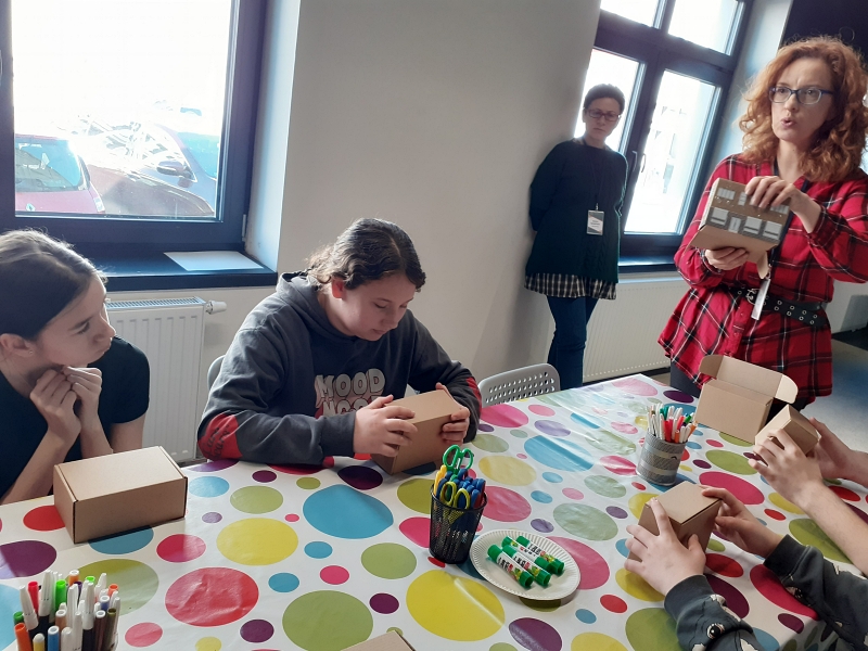 Pani edukator pokazuje uczniom wzór domu, jaki mają sami zaprojektować.