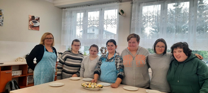 Zdjęcie przedstawia uczestników programu z grupy dziewcząt wraz z prowadzącą zajęcia p Beatą Drzymałą pozujących w pracowni gospodarstwa domowego przy gotowej do spożycia sałatce z kaszy pęczak jajek i nowalijek [800x360]
