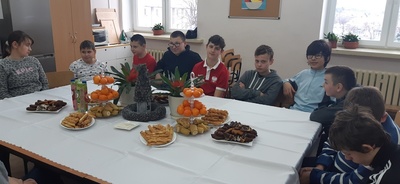 Uczniowie rożnych klas siedzą w szkolnej kuchni, przy wigilijnym stole. 