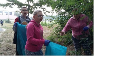 Uczniowie klasy ósmej zbierają śmieci w lasku koło szkoły.