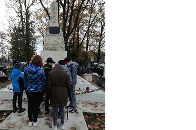 Dziewczynki i chłopcy stoją przed grobem poległych żołnierzy i zapalają znicze.