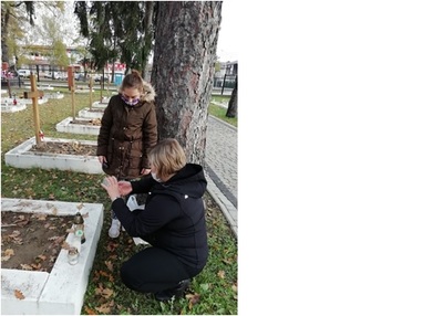 Pani Basia zapala znicze przy grobie żołnierza, obok niej stoi uczennica.