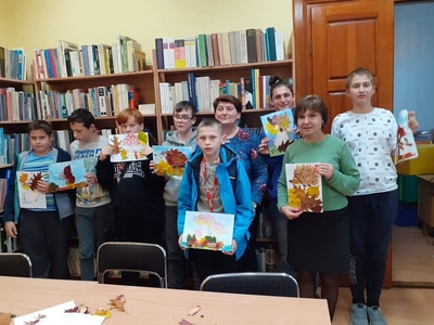 Zdjęcie przedstawia całą grupę wraz z wychowawczynią i bibliotekarką. Wszyscy trzymają prace plastyczne wykonane z liści.