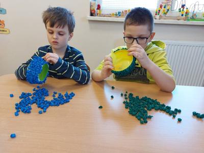 Na zdjęciu chłopcy, wyklejają miseczki kolorowymi kulkami z bibuły.