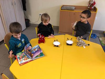Przedszkolaczki siedzą przy stole. Jeden z nich ogląda kolorową ksiązkęa pozostali prezentują
zrobione prace.