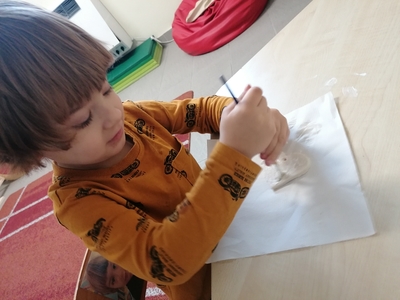 Jeden z przedszkolaczków smaruje klejem serduszko z masy solnej.