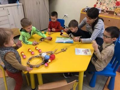 Pani Natalia i jej oddział. Wszyscy grzecznie siedzą przy stole. Pani czyta wiersz a na stole prezentują
się instrumenty.