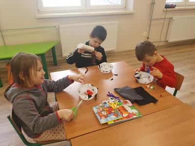 Dzieci siedzą przy stole i ozdabiają miseczki dla kotków