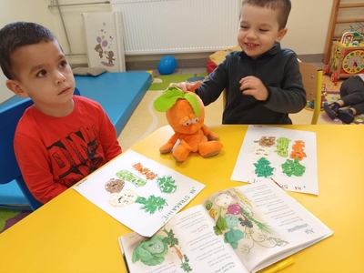 Przy stole siedzą chłopcy, maja przed sobą prace przedstawiające warzywa.