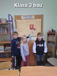 Wiktor uśmiechnięty wskazuje palcem przyklejony herb. Towarzyszy mu Madzia.