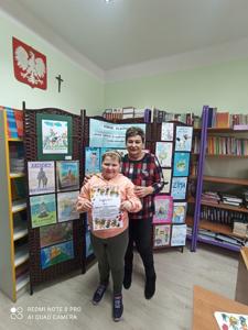 Uśmiechnięta Wiktoria z Panią Wicedyrektor. W tle prace konkursowe.