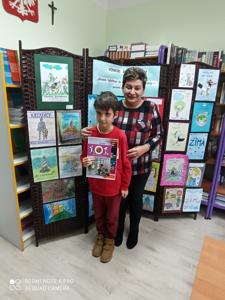 Dumny Adaś odbiera dyplom i nagrodę za zajęcie 1 miejsca w konkursie plastycznym. Na zdjęciu z Panią Wicedyrektor a w tle przepiękne prace plastyczne. 