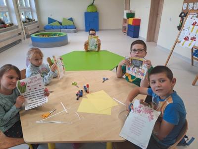 Dzieci siedzą przy stole i trzymają wykonane prace. 